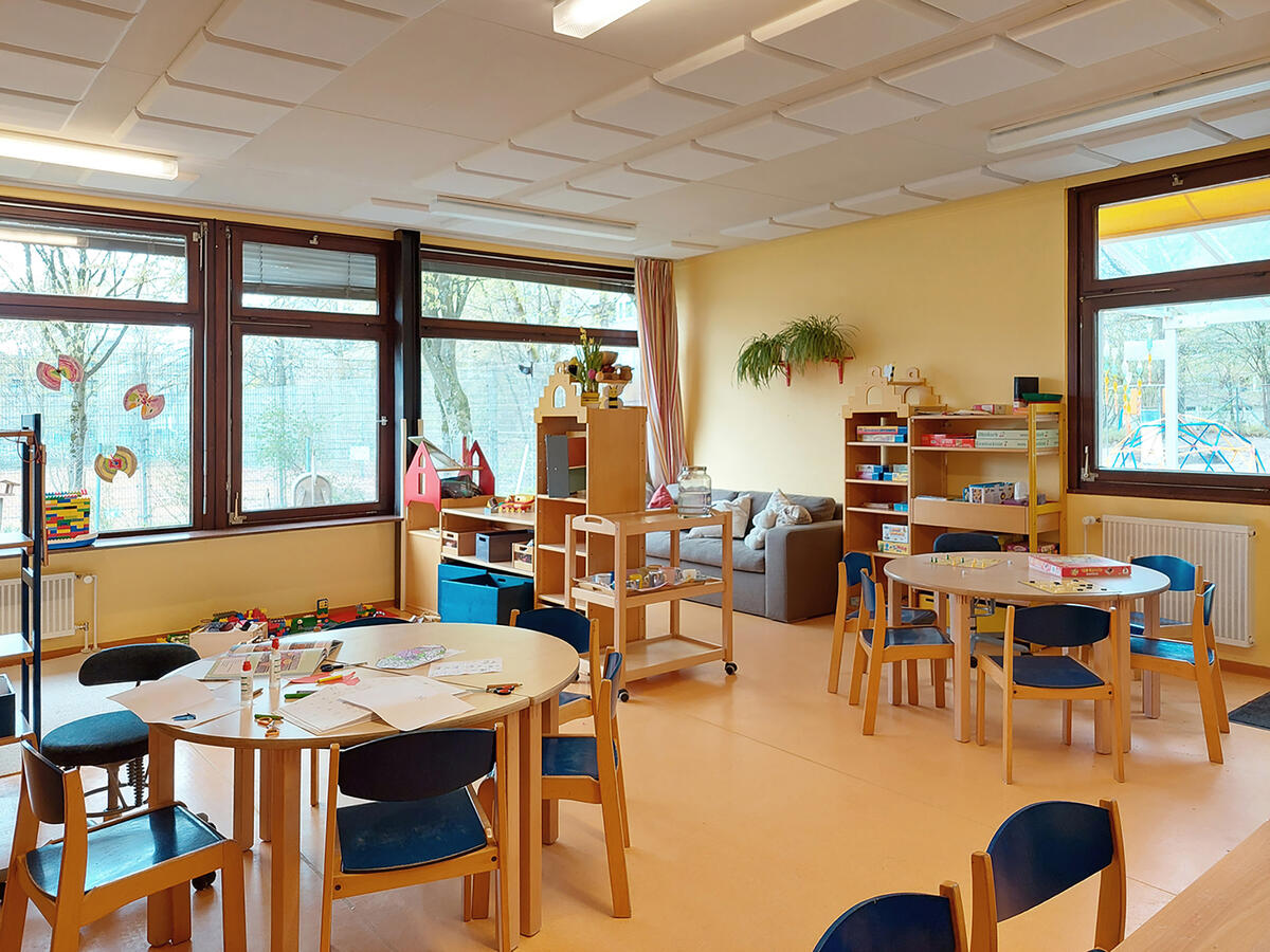Gruppenraum im Kinderhaus Uni-Kids mit mehreren Tischen, einer Couch und verschiedenen Spielen