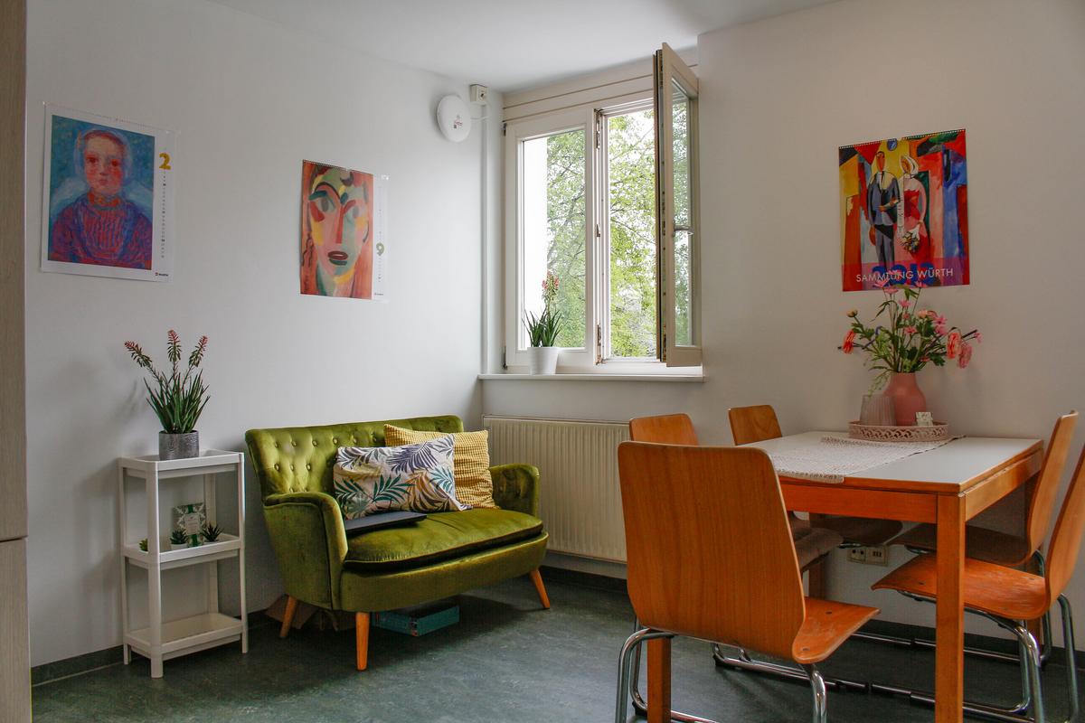 Living area: A small green sofa and a table with four chairs. Expressionist paintings hang on the walls.