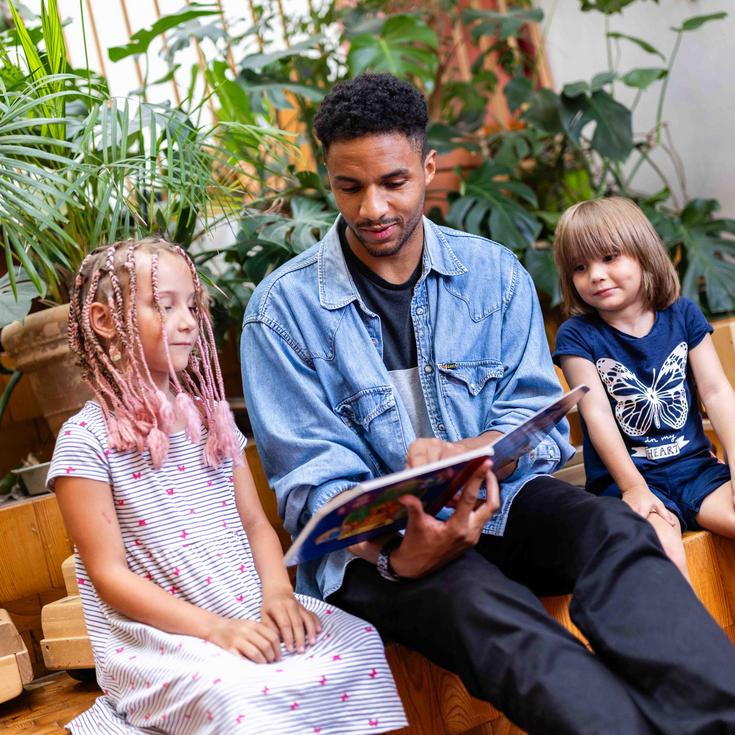 Erzieher liest zwei Kindern aus einem Buch vor.
