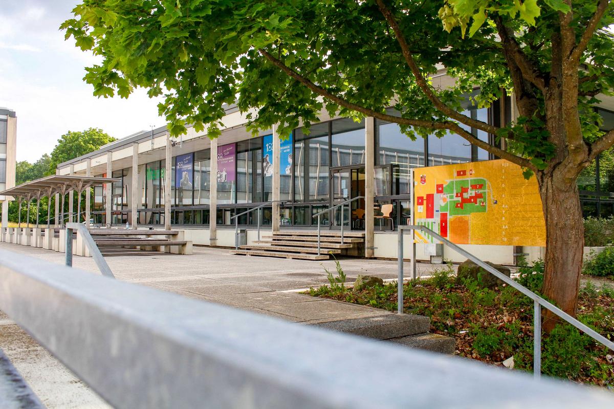 Außenansicht der Mensa in Ludwigsburg mit gläsernen Fronten. Im Vordergrund ist rechts ein Schild und ein Baum zu sehen