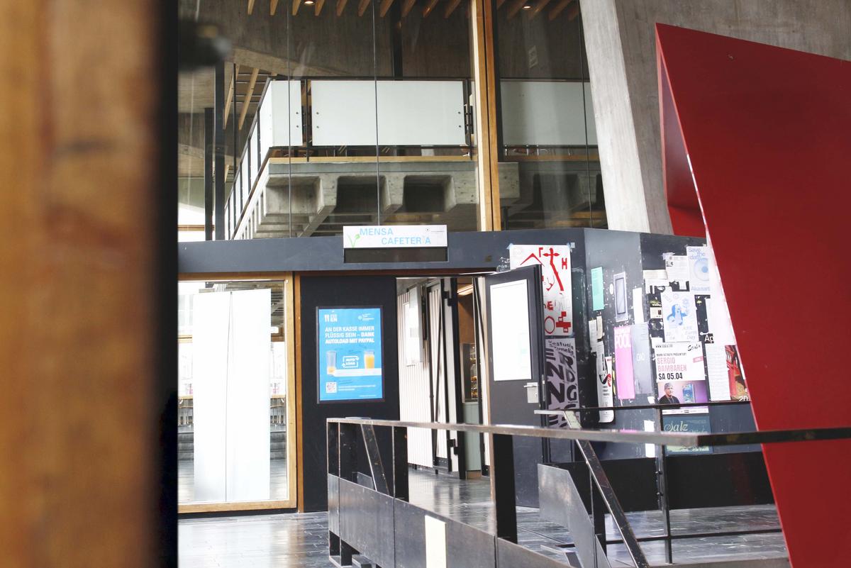 Entrance area of the Kunstakademie canteen. To the left of the entrance is a screen with information about Autoload. A sign ‘Mensa Cafeteria’ hangs above the door