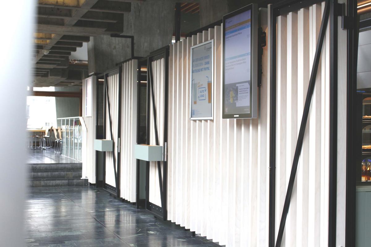 Cash desk area of the art academy. On the right are numerous white boards separating the cash desk area from the corridor. There is a screen and a poster on the boards.
