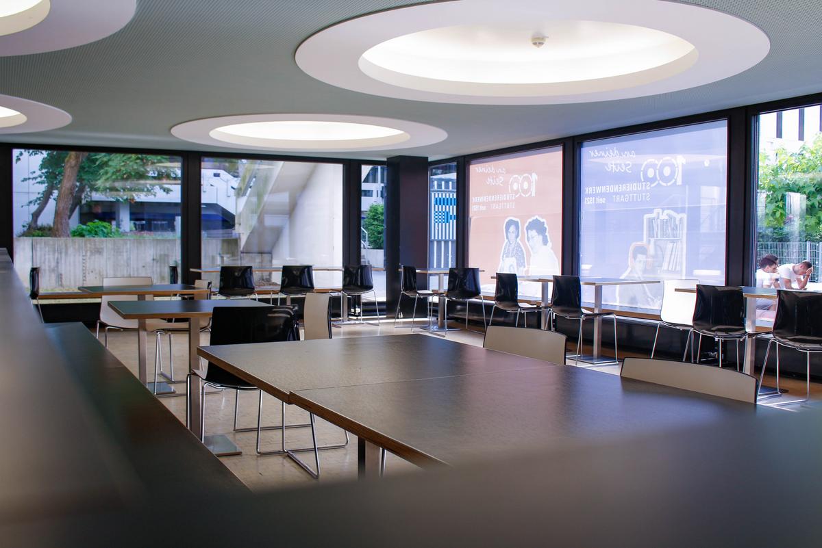Innenraum der Cafeteria Lichtblick. Tische mit schwarzen Stühlen und großen runden Deckenleuchten